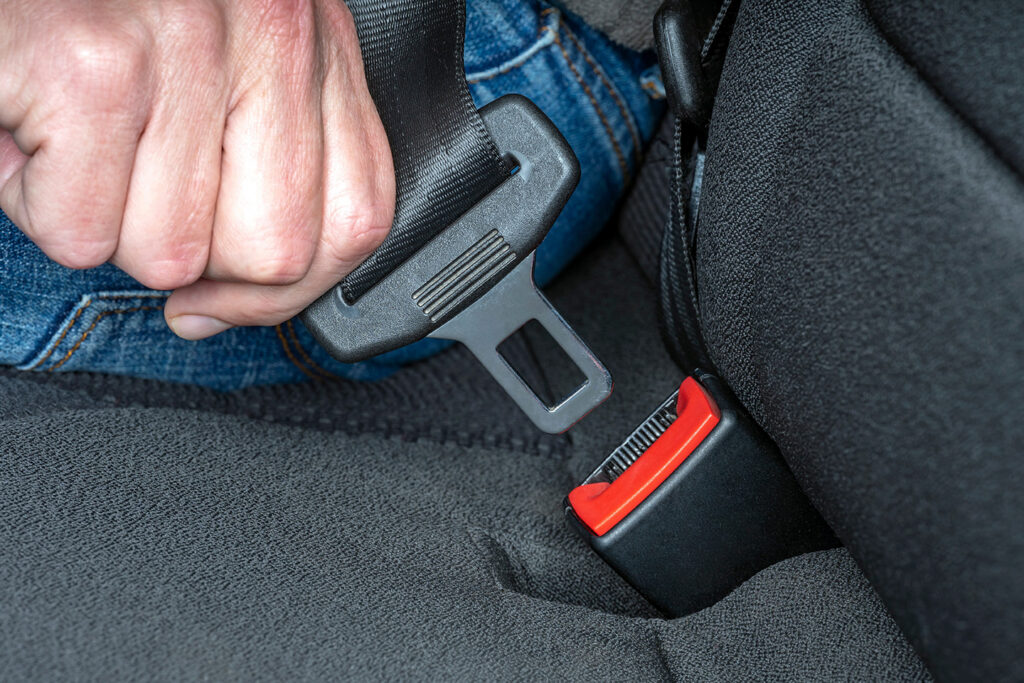 person putting on seat belt in car